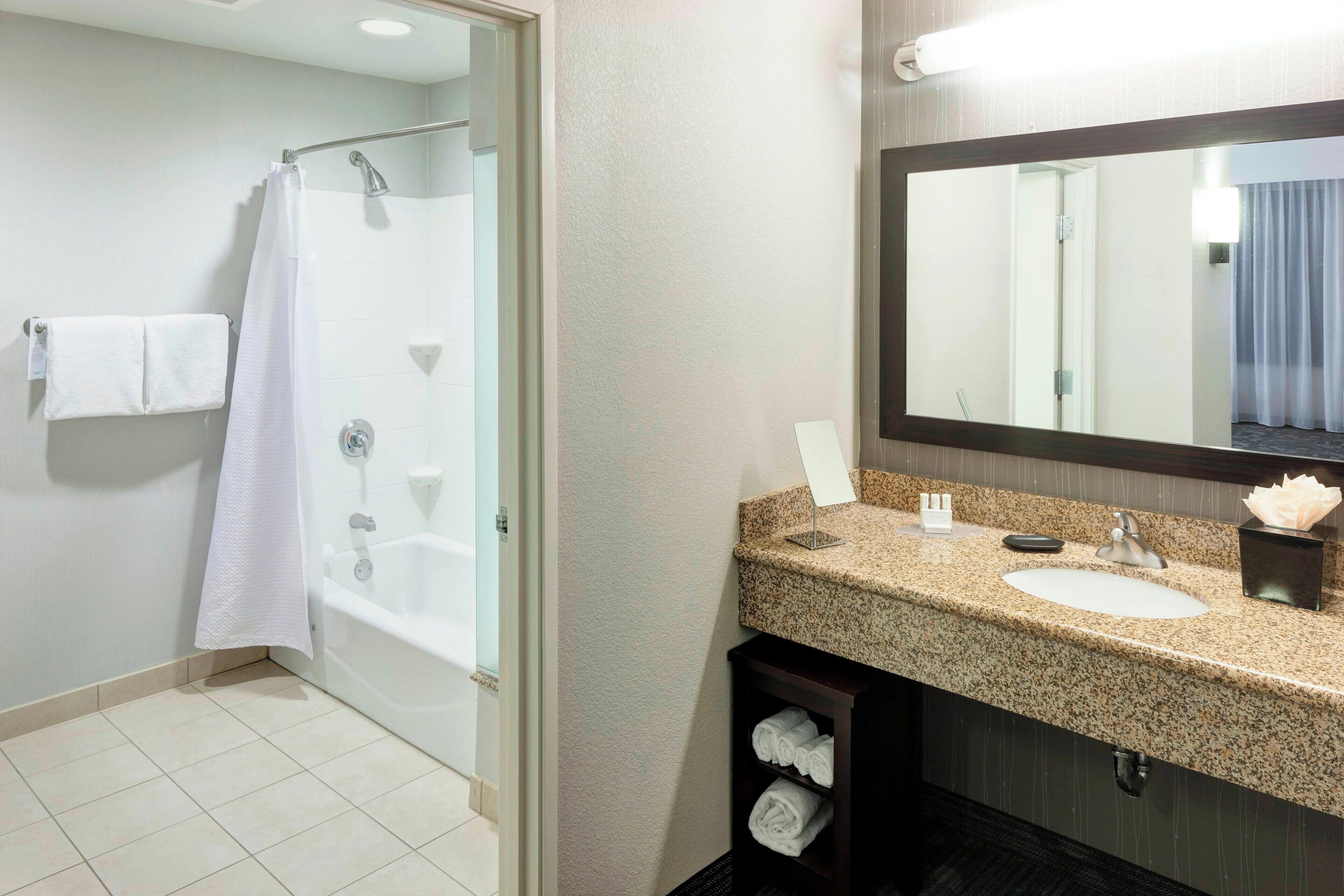 Une salle de bain moderne avec une douche en verre, un lavabo doté d’un plan de travail en granit et un grand miroir.