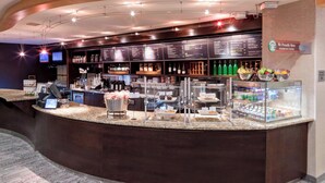 Un área de bar moderna con una barra curva, carteles con la carta y una variedad de bebidas y aperitivos a la vista.