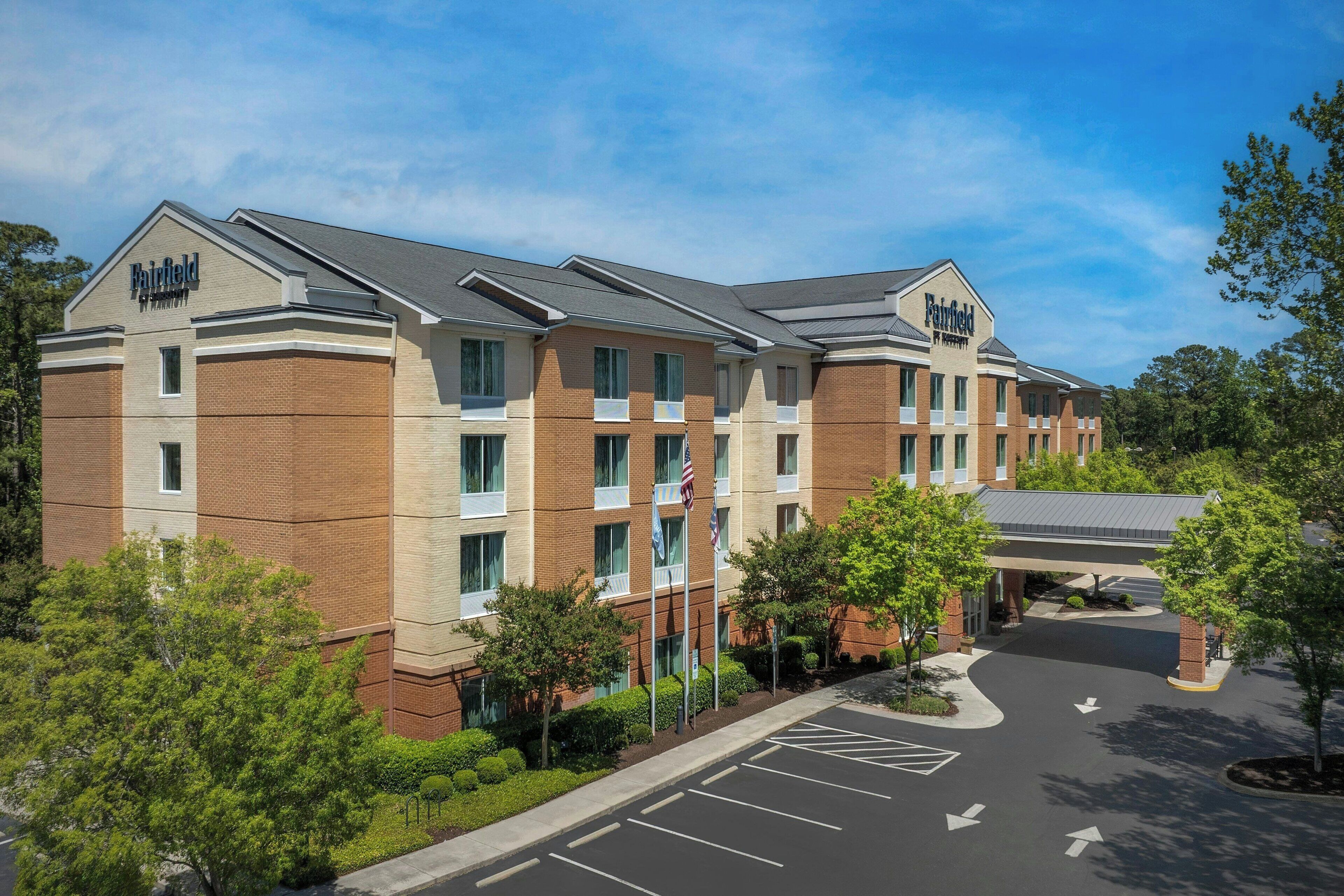 A multi-story hotel with a brick facade, multiple windows, and a parking lot with directional arrows.