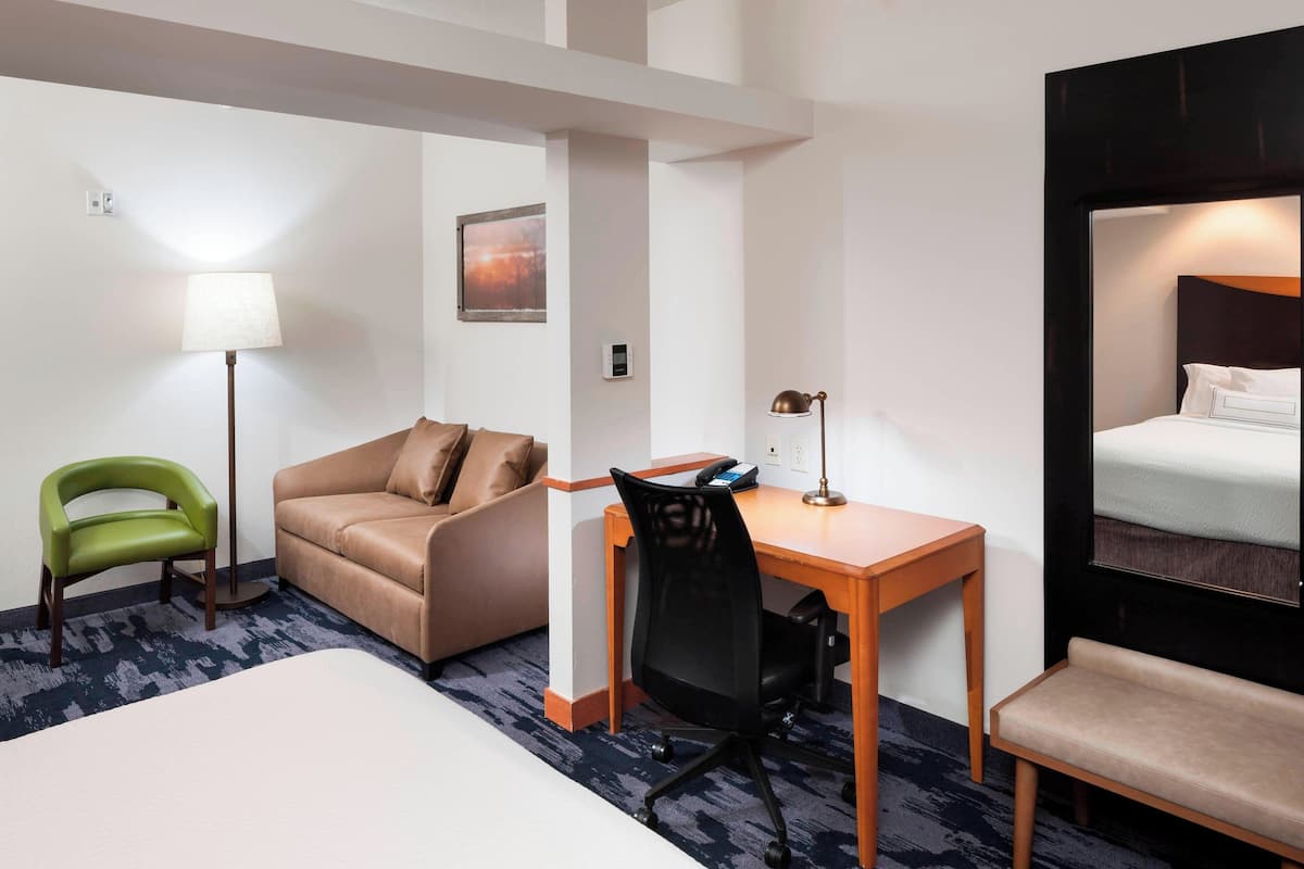 Hotellihuone, jossa on sänky, työpöytä tuolilla, sohva, vihreä tuoli ja lamppu.