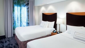 A hotel room with two beds, a nightstand with a lamp, and a view of a forest through the window. - Fairfield Inn & Suites by Marriott Wilmington/Wrightsville Beach (Wilmington)