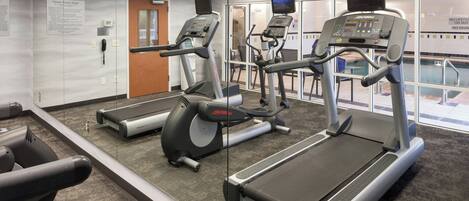 Un gimnasio con cintas de correr, bicicletas estáticas y un espejo grande.