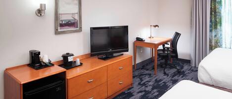 A hotel room with a bed, a desk with a chair, a television, a coffee maker, and a small refrigerator.