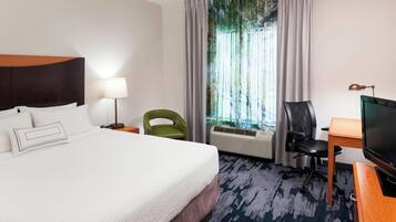 A hotel room with a large bed, a desk with a computer, a chair, a lamp, and a window with curtains.