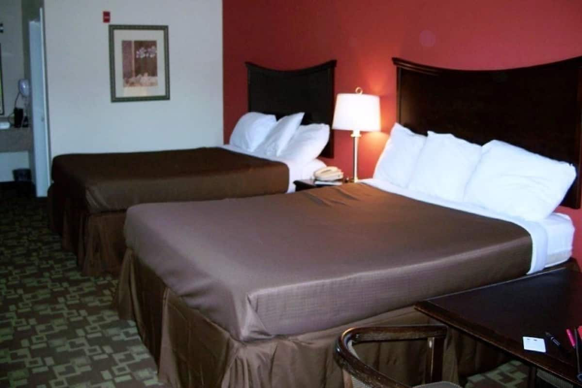 Een hotelkamer met twee bedden, een bureau, een stoel, een lamp en een lijst aan de muur.