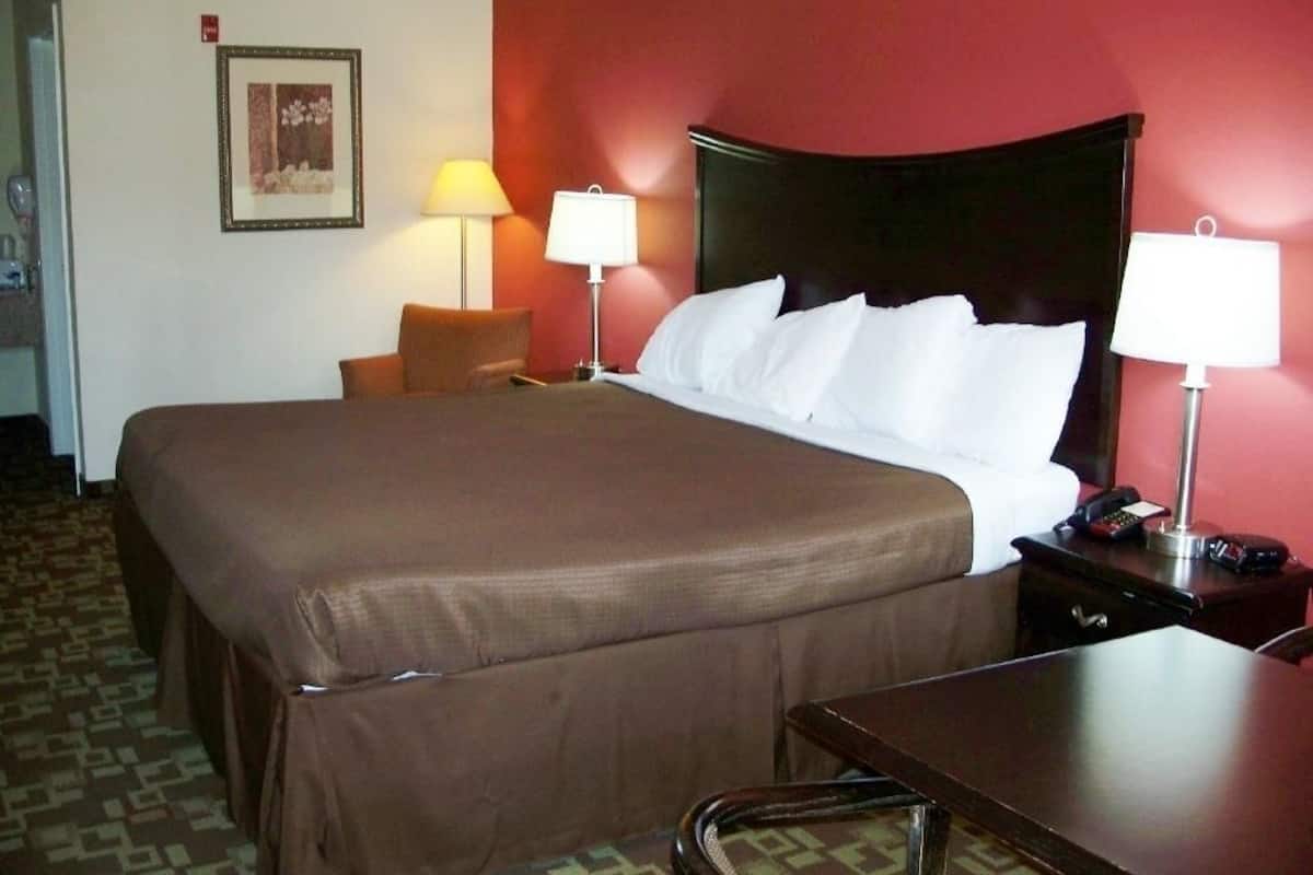 Een hotelkamer met een groot bed, twee bedlampen, een nachtkastje met een telefoon en een stoel.