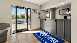 A reception area with a blue mat, a grey couch, and a view of the outdoors. - Americas Best Value Inn Byhalia (Byhalia)