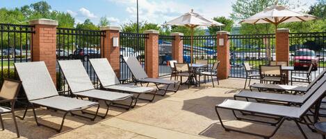 An outdoor patio area with lounge chairs and umbrellas, surrounded by a brick wall and metal fence.