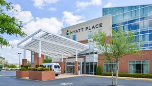 A modern Hyatt Place hotel with a covered entrance, a parking area, and a landscaped garden.