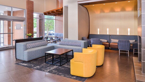 A modern lobby with a grey sofa, yellow armchairs, and a wooden coffee table.