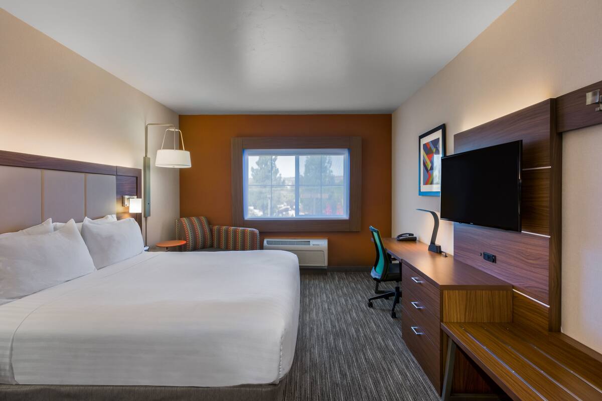 A hotel room with a large bed, a desk with a flat-screen TV, a window with a view, and a wall-mounted air conditioner.