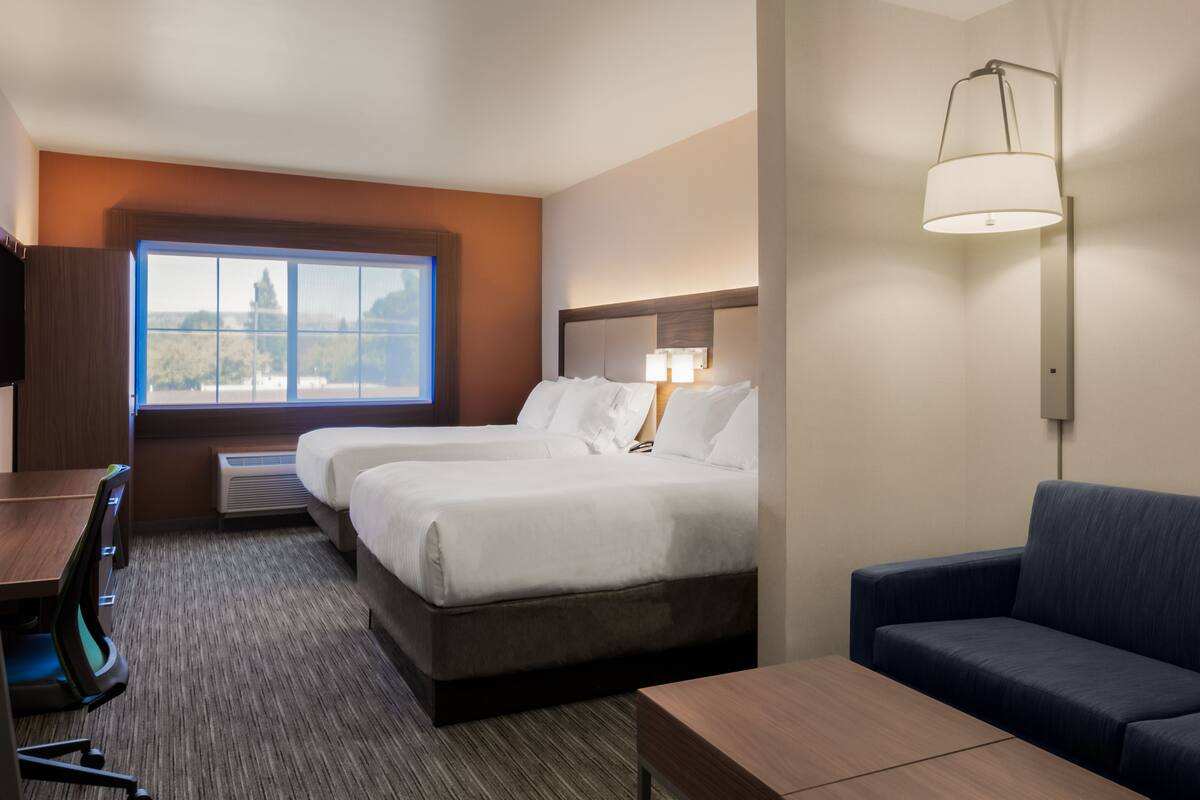 A hotel room with two beds, a desk, a chair, a sofa, and a window with a view.