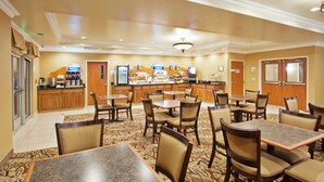 Un comedor de hotel con varias mesas y sillas, un mostrador de buffet y una estación de café.
