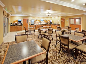 Un comedor de hotel con varias mesas y sillas, un mostrador de buffet y una estación de café.