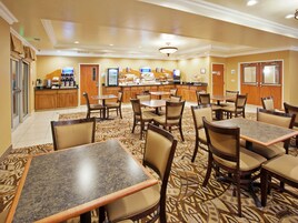 Un comedor de hotel con varias mesas y sillas, un mostrador de buffet y una estación de café.