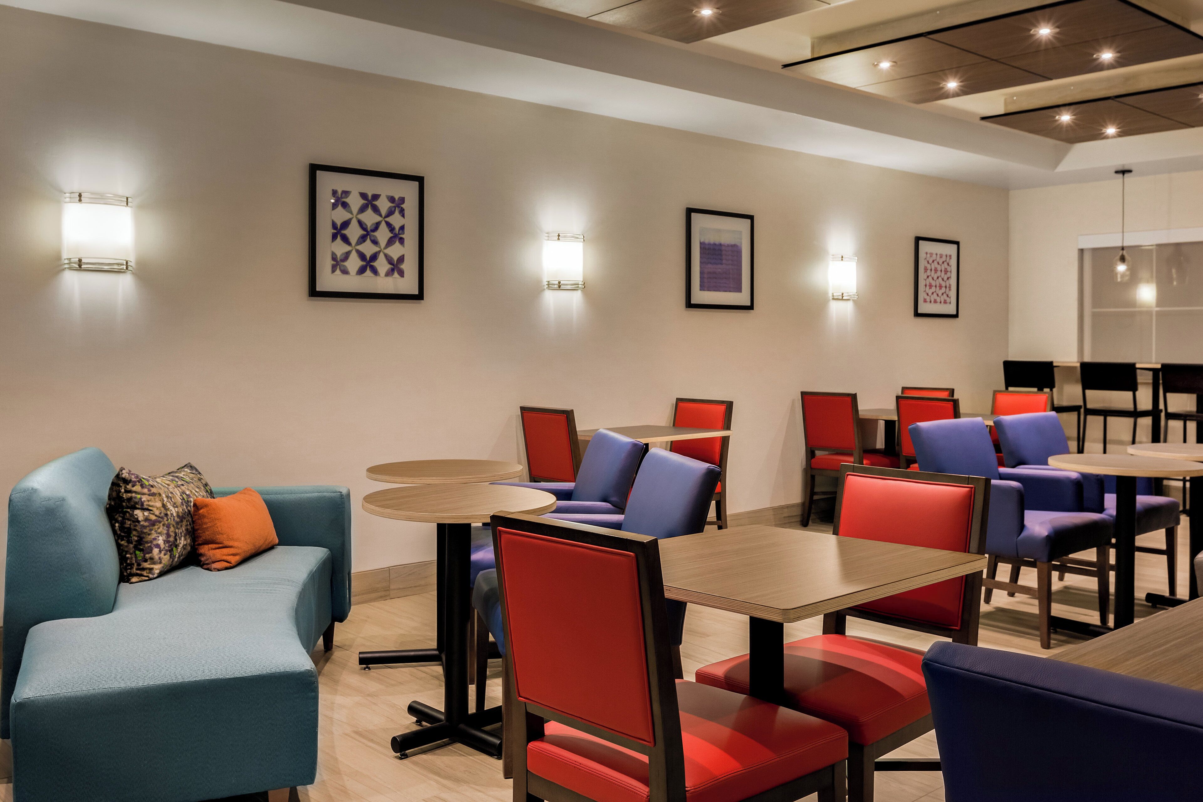 A hotel dining area with multiple tables and chairs, some with red and blue upholstery.