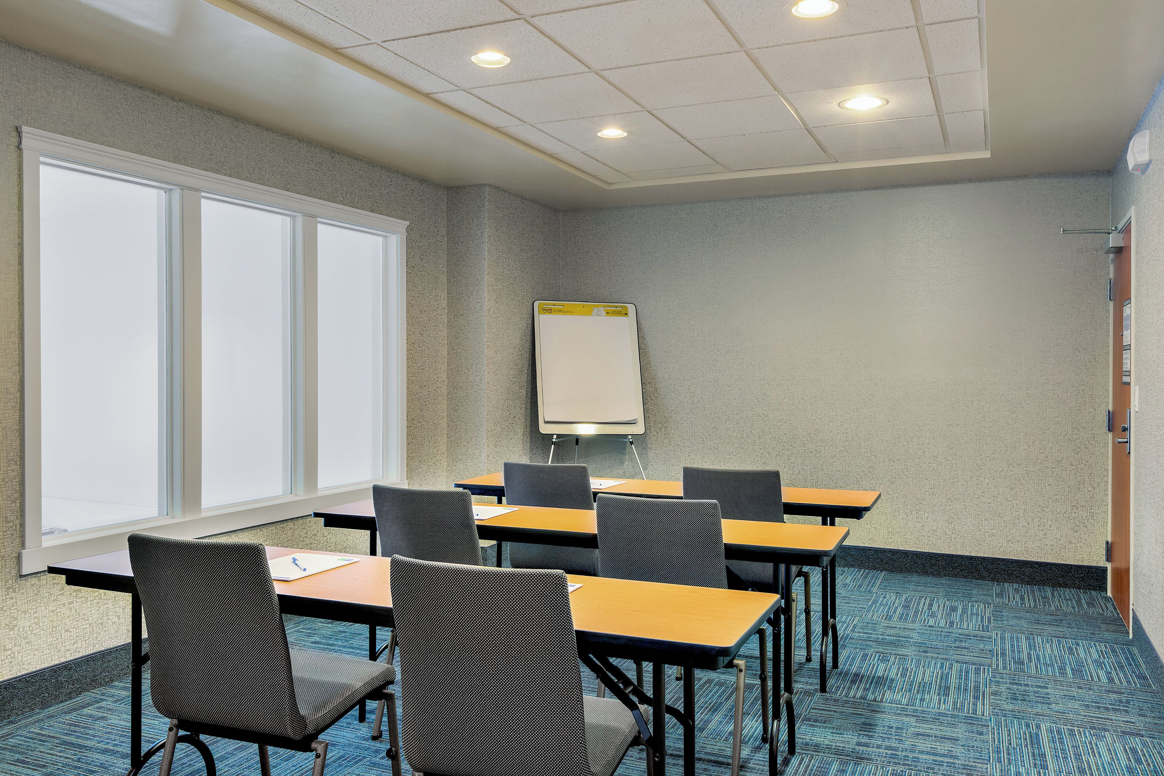 Une salle de conférence équipée d’un tableau blanc, de plusieurs tables et de chaises.