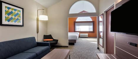 A hotel room with a sofa, a small table, a TV, a bed, and a window with a view.