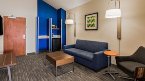 A hotel room with a blue accent wall, a sofa, a small table, a lamp, and a TV.