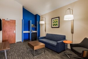 Habitación de hotel con pared de acento azul, un sofá, una mesita, una lámpara y un televisor.