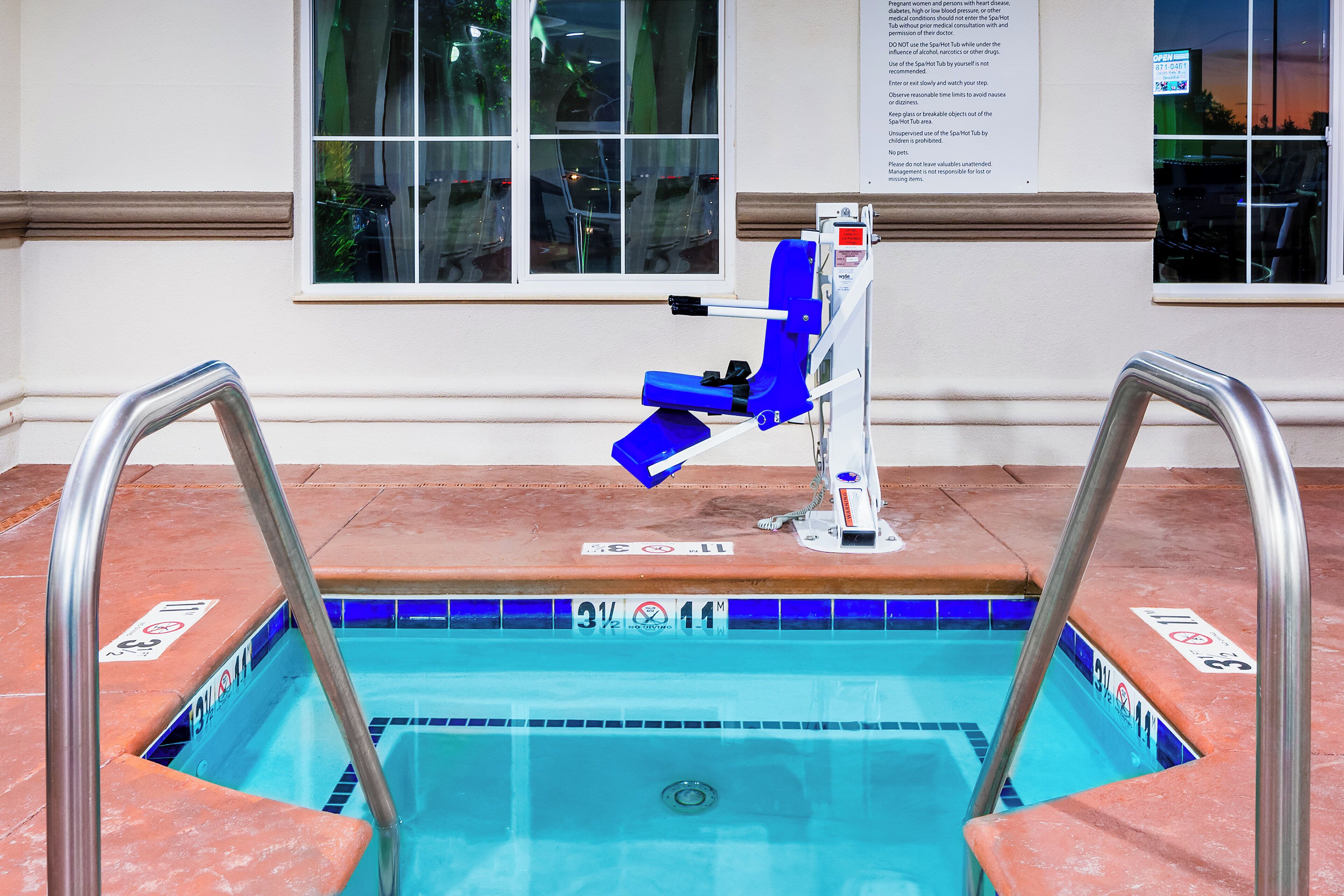 A pool with a blue tiled edge, a safety ladder, and a sign with instructions.