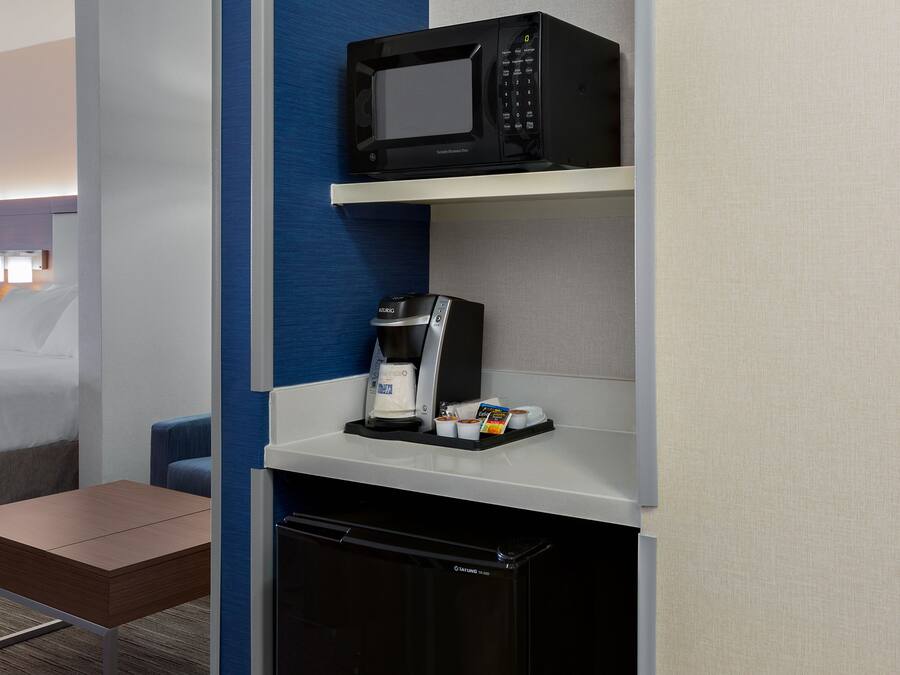 Ein kompaktes Hotelzimmer mit Küchenzeile, inklusive Mikrowelle, Kaffeemaschine und kleinem Kühlschrank.