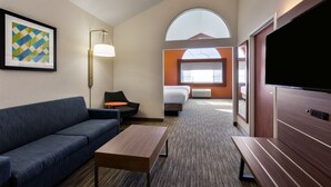 A hotel room with a sofa, a small table, a TV, a bed, and a window.
