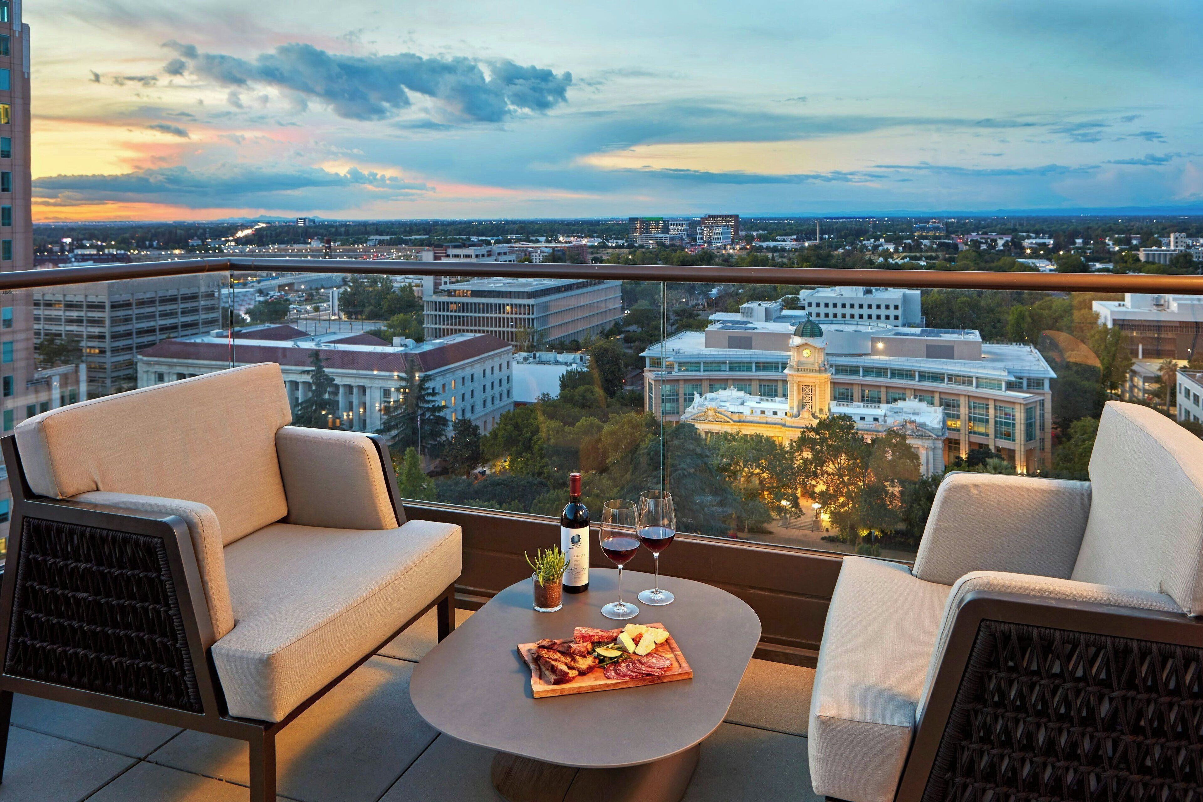 Un balcon avec deux canapés, une table sur laquelle se trouvent une bouteille de vin, des verres et un plateau de nourriture.