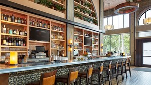 A bar area with multiple shelves of liquor bottles, a flat-screen TV, and bar stools. - The Citizen Hotel, Autograph Collection (Sacramento)