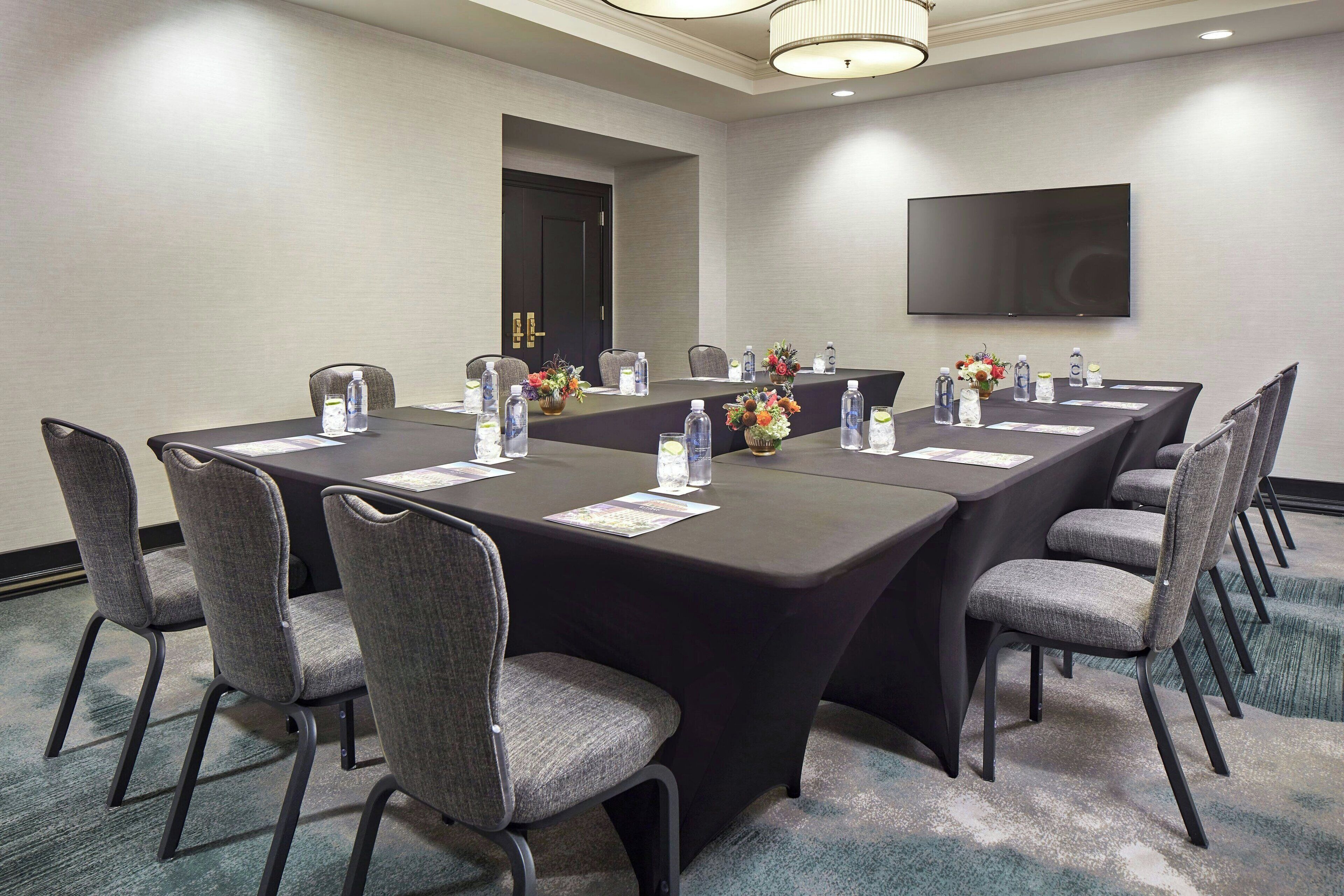 A conference room with a long table, chairs, water bottles, and a flower arrangement.