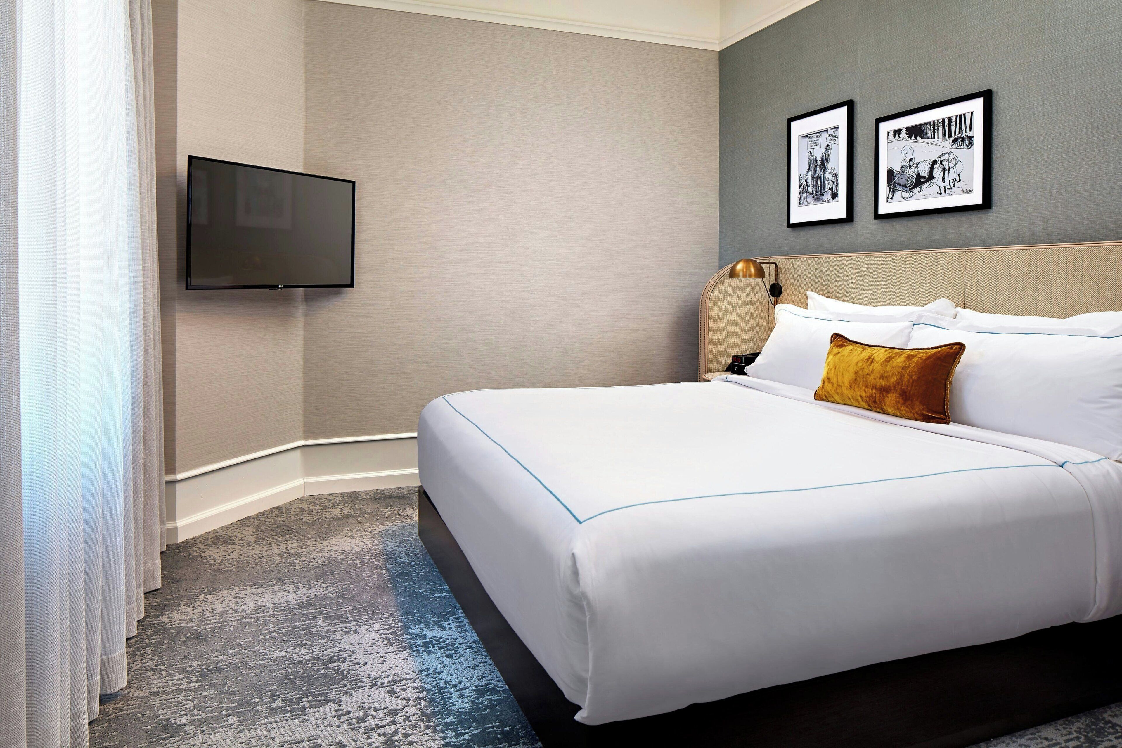 A hotel room with a large bed, a flat-screen TV mounted on the wall, and two framed pictures above the bed.