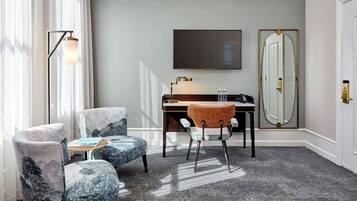 A hotel room with a large window, a desk with a chair, a large mirror, and a sofa.