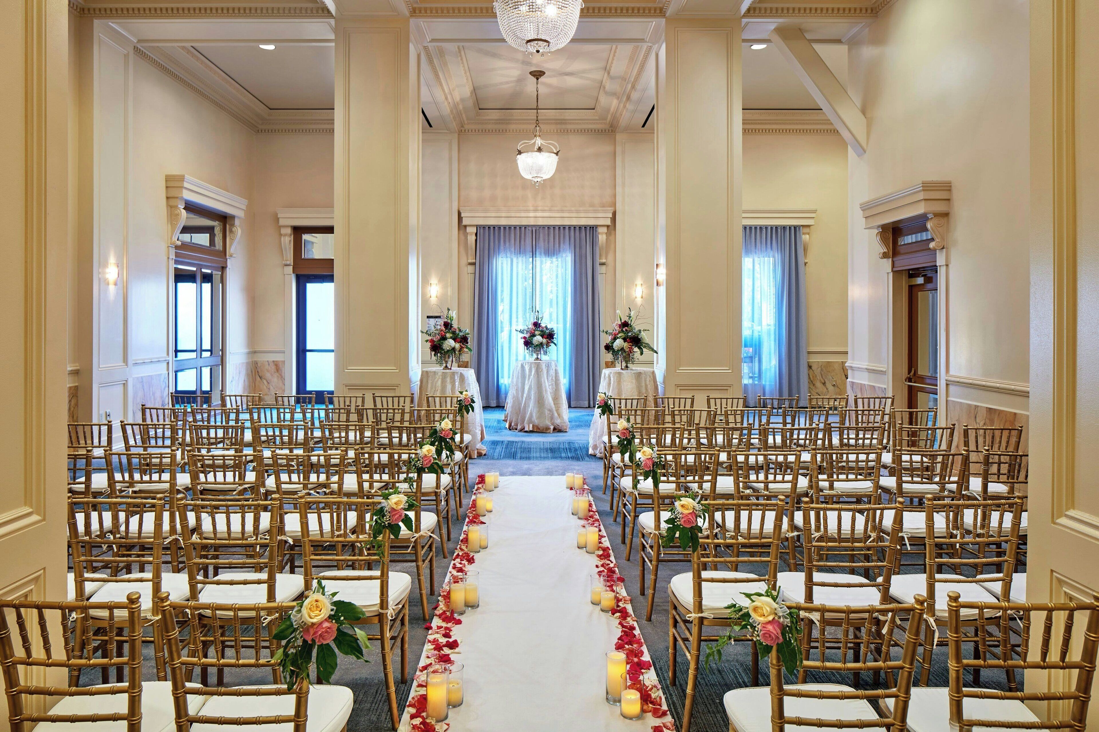 A formal indoor setting with rows of chairs arranged for an event, a central aisle, and floral decorations.