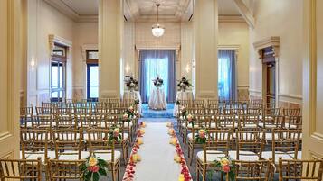 A formal indoor setting with rows of chairs arranged for an event, a central aisle, and floral decorations.