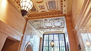 A grand lobby with ornate ceiling decorations, a large chandelier, and a grand entrance with a black door.