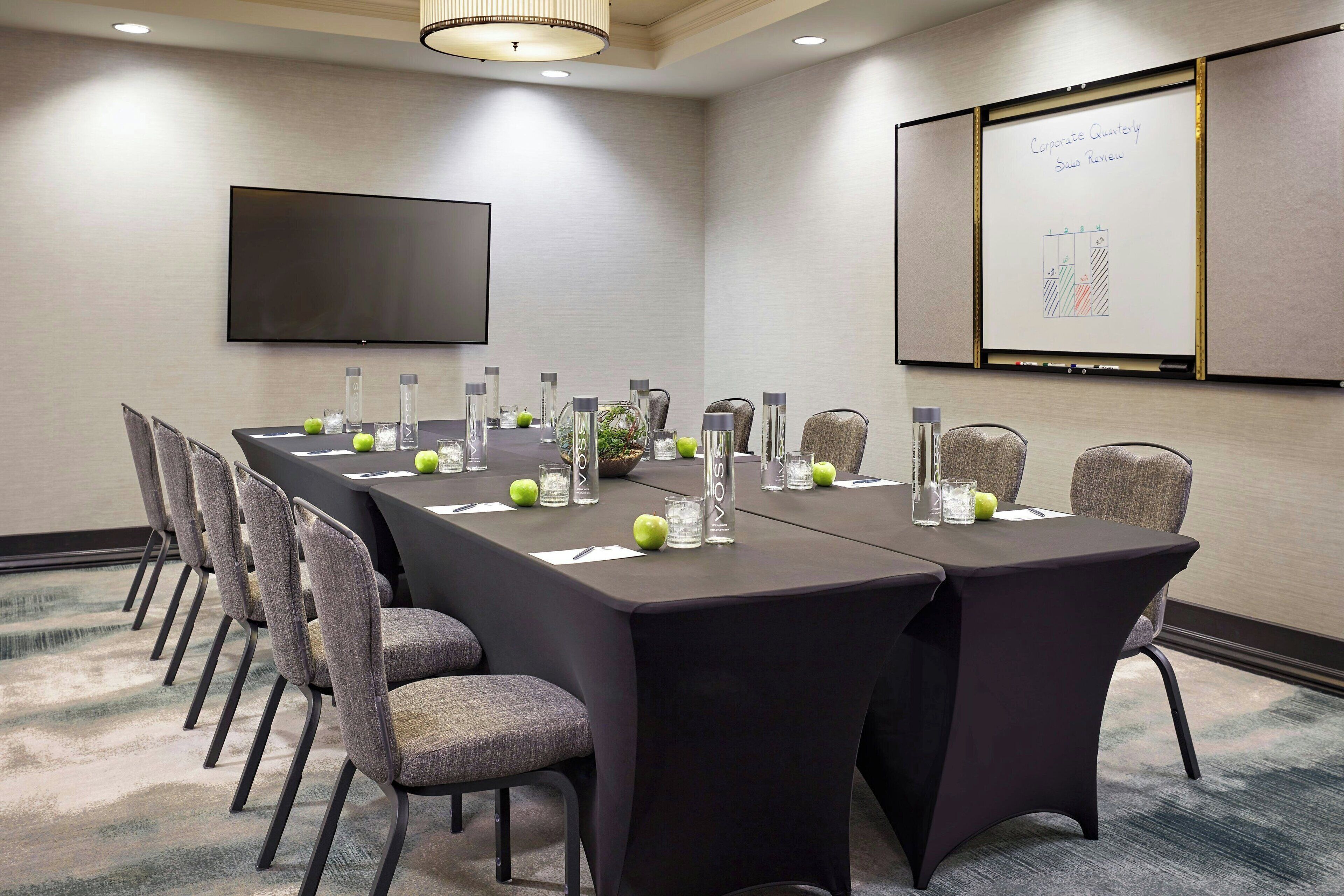 A conference room with a long table, chairs, a TV, and a whiteboard with a chart.