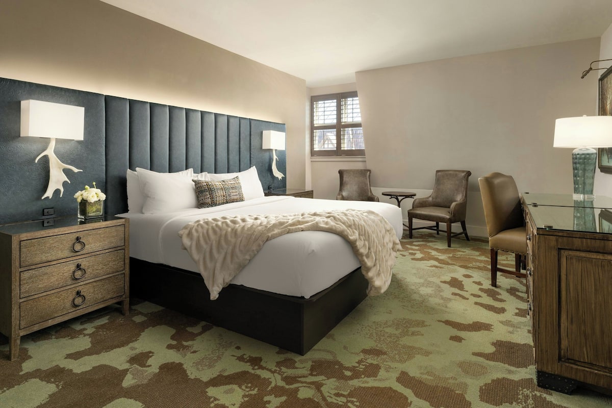 Une chambre d’hôtel avec un grand lit, une table de chevet avec des tiroirs, une chaise, un bureau et une fenêtre.