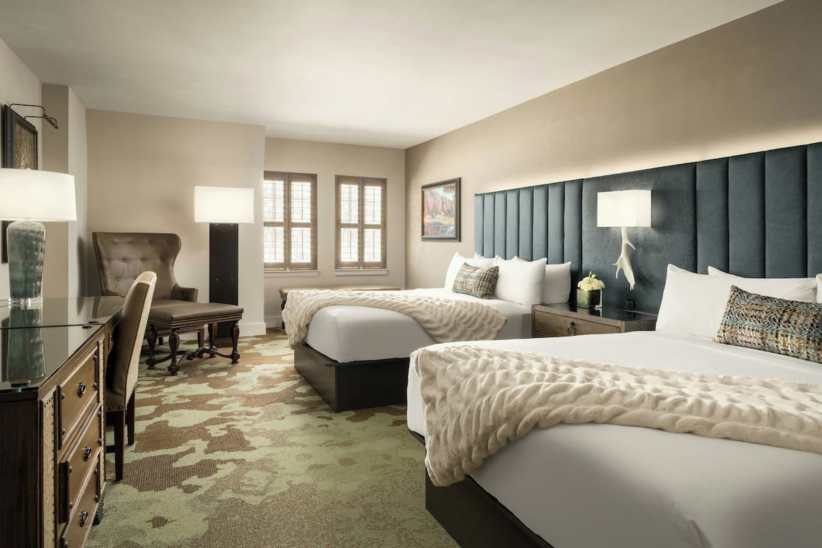 Une chambre d’hôtel avec deux lits, un bureau, une chaise et une grande fenêtre.