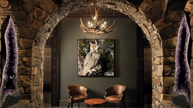 Una habitación de paredes de piedra con un candelabro, dos sillones de cuero y un cuadro en la pared.
