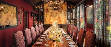 A formal dining room with a long table set for a meal, surrounded by upholstered chairs.