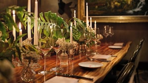 Una mesa de comedor dispuesta con velas, copas y platos, con una cabeza de ciervo montada en la pared de fondo.