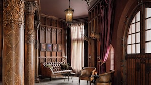 Una habitación con columnas de madera decoradas, un sofá de cuero, un sillón estampado y un amplio ventanal arqueado.