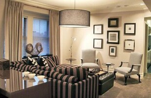 A living room with striped sofas, a glass coffee table, a floor lamp, and framed pictures on the wall.