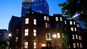A historic building with multiple windows and a prominent corner turret, surrounded by modern high-rise buildings. - The Inn At St Botolph (Boston)