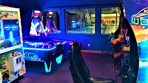 Un salón de juegos con máquinas recreativas iluminadas con neón, una mesa de billar y un área de descanso.