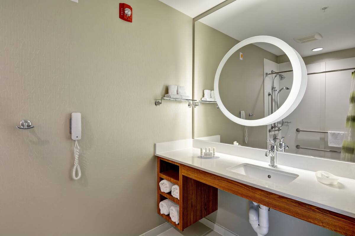 A modern bathroom with a white sink, a large mirror, and a wooden vanity.