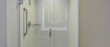 A glass-enclosed shower with a door, a handrail, and a showerhead.