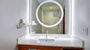 A modern bathroom with a white vanity, a round mirror, and a glass shower enclosure.