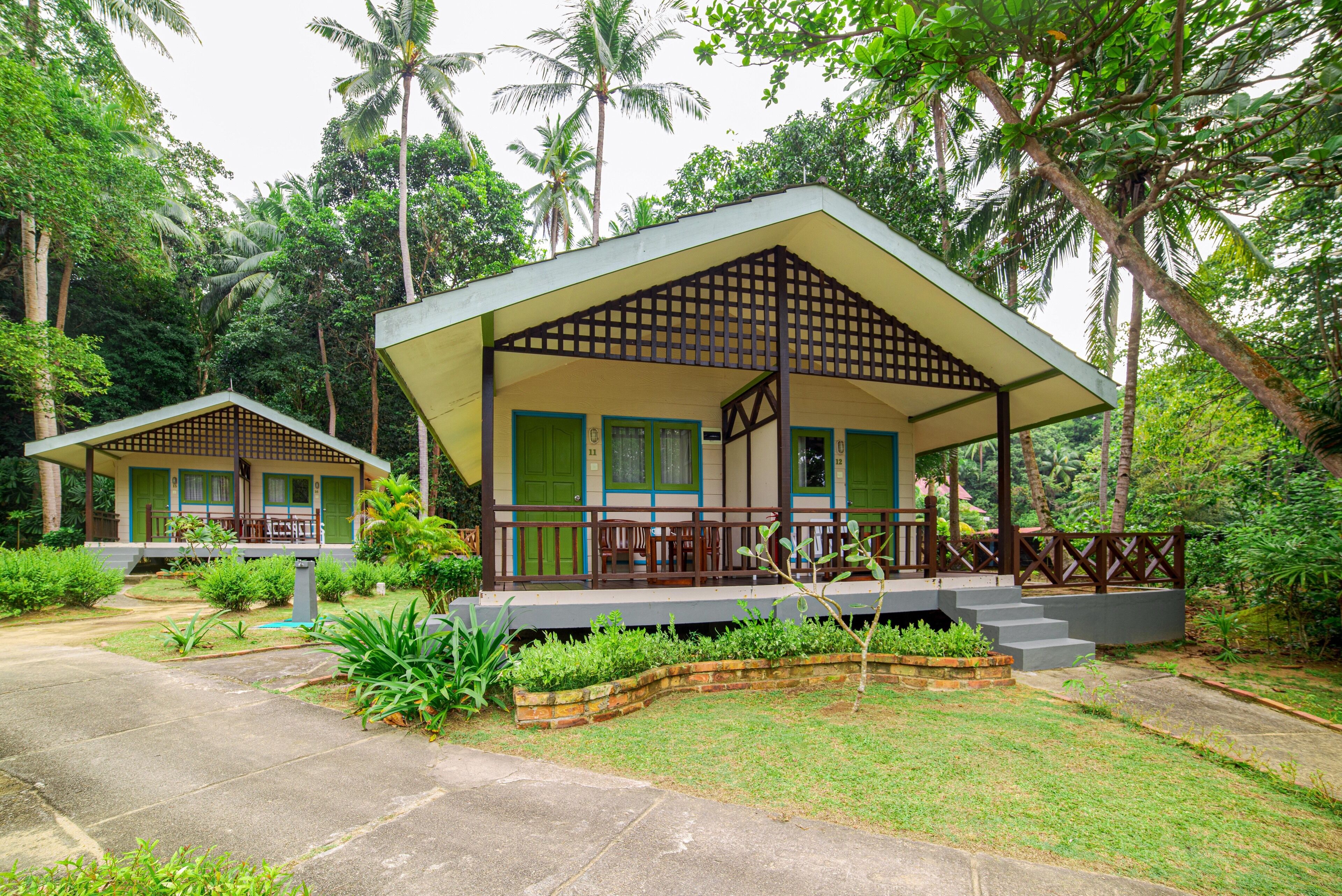 A bungalow with a covered porch, surrounded by lush greenery and palm trees.
