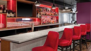 Een bar met een marmeren aanrecht, rode barstoelen en planken vol met verschillende flessen en glazen.